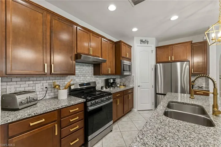 Kitchen featuring pendant lighting, backsplash, light tile floors, sink, and appliances with stainless steel finishes