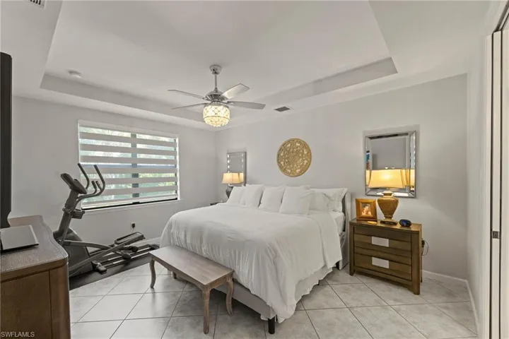 Primary Tiled bedroom featuring ceiling fan and tray ceiling