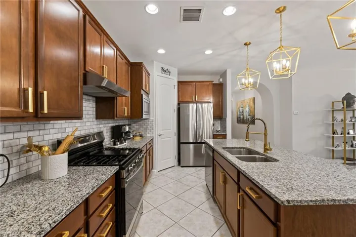 Kitchen with stainless steel appliances, wall chimney exhaust hood, sink, tasteful backsplash, and light tile flooring