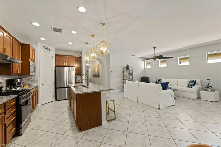 Kitchen with a center island with sink, ceiling fan with notable chandelier, appliances with stainless steel finishes, light stone counters, and tasteful backsplash