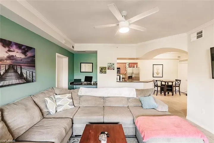 Living area featuring arched walkways, ornamental molding, and ceiling fan