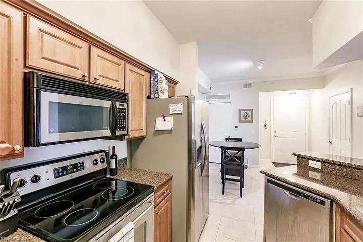 Kitchen with stainless steel appliances, dark stone counters, crown molding, and light tile patterned floors