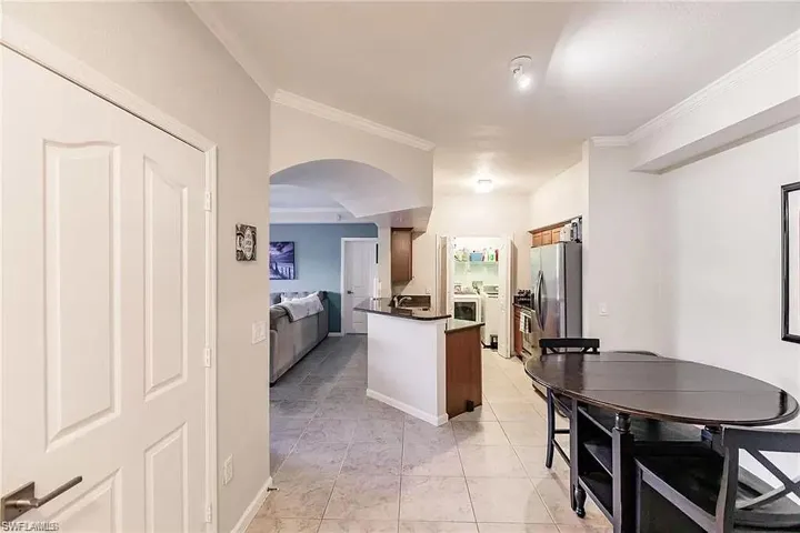 Kitchen with dark countertops, arched walkways, crown molding, light tile patterned floors, and stainless steel fridge