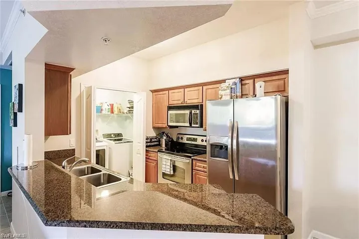 Kitchen with appliances with stainless steel finishes, washer and dryer, a peninsula, dark stone countertops, and tile patterned flooring