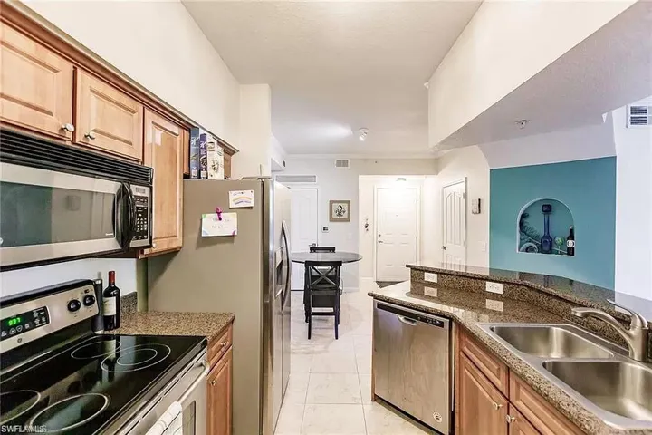 Kitchen with stainless steel appliances, light tile patterned floors, stone counters, ornamental molding, and light brown cabinetry