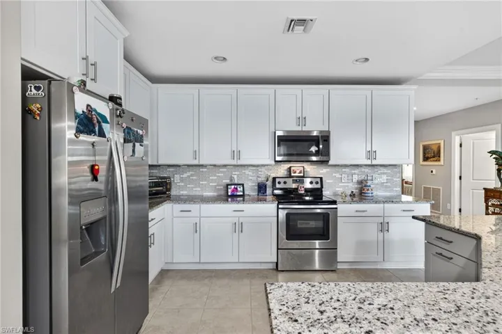 Kitchen featuring appliances with stainless steel finishes, white cabinets, light stone countertops, light tile patterned floors, and recessed lighting
