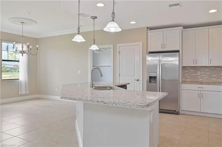 Kitchen island with stone countertop, stainless steel appliances, white cabinetry, tile backsplash, and recessed lighting