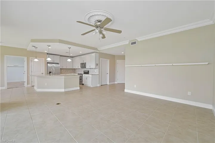 Open-concept living area featuring large format tile flooring, crown molding, and a kitchen with white cabinetry