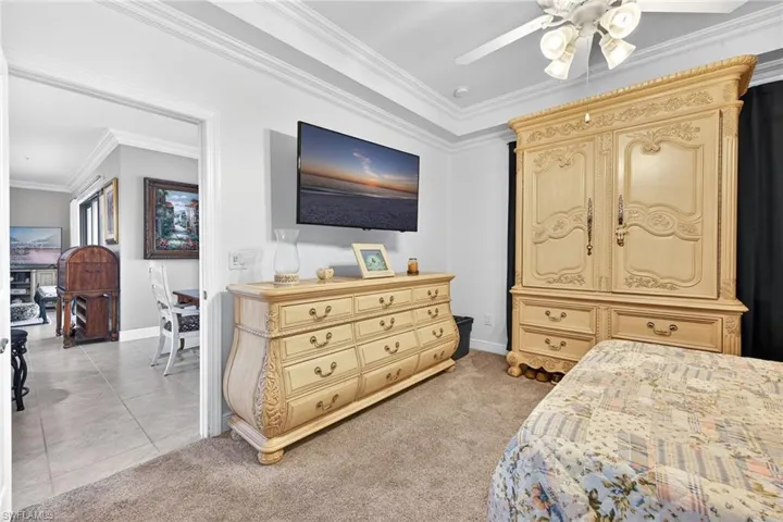 Bedroom with ornamental molding, light colored carpet, ceiling fan, and light tile patterned floors