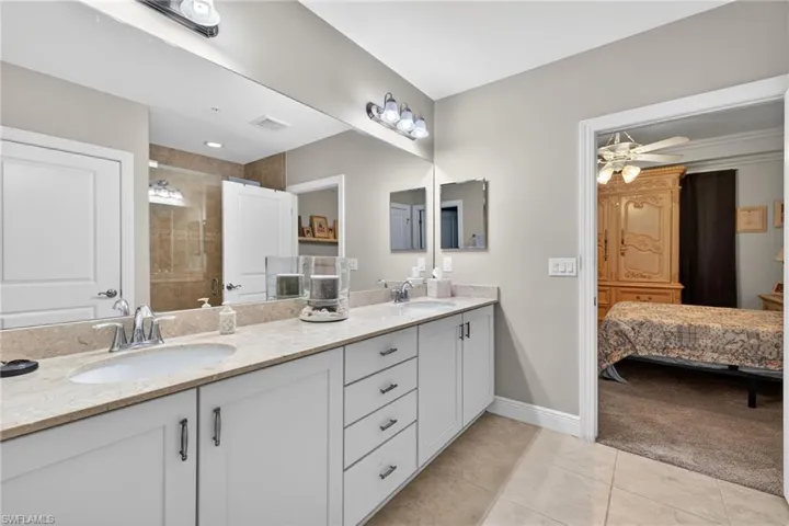 Ensuite bathroom with double vanity, light tile patterned floors, a tile shower, and light colored carpet