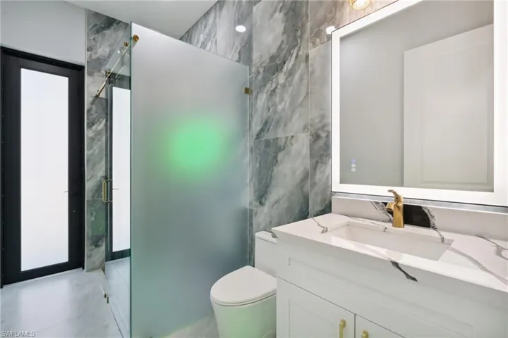 Bathroom with an enclosed shower, vanity, toilet, and tile walls