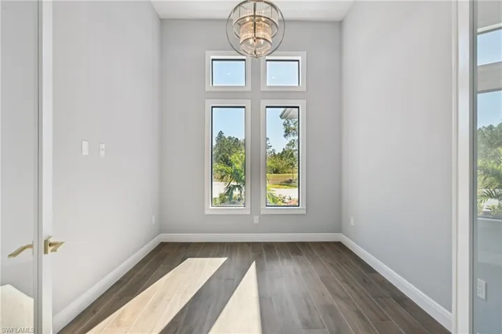 Unfurnished room with dark hardwood / wood-style flooring, a wealth of natural light, and a notable chandelier