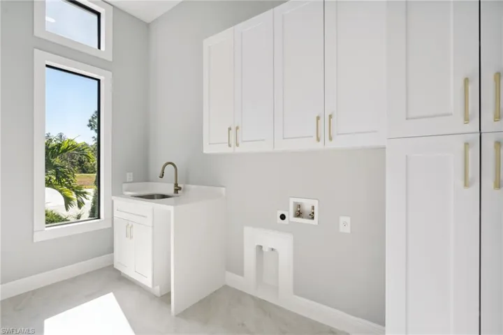 Clothes washing area featuring electric dryer hookup, a wealth of natural light, sink, and cabinets