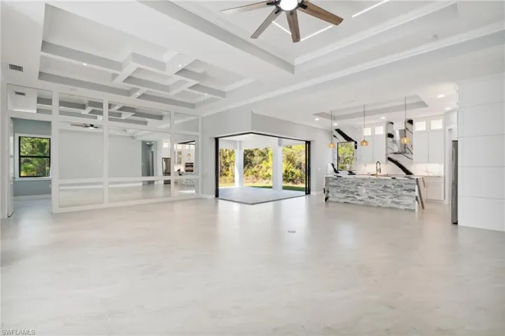 Unfurnished living room featuring ceiling fan, ornamental molding, and coffered ceiling