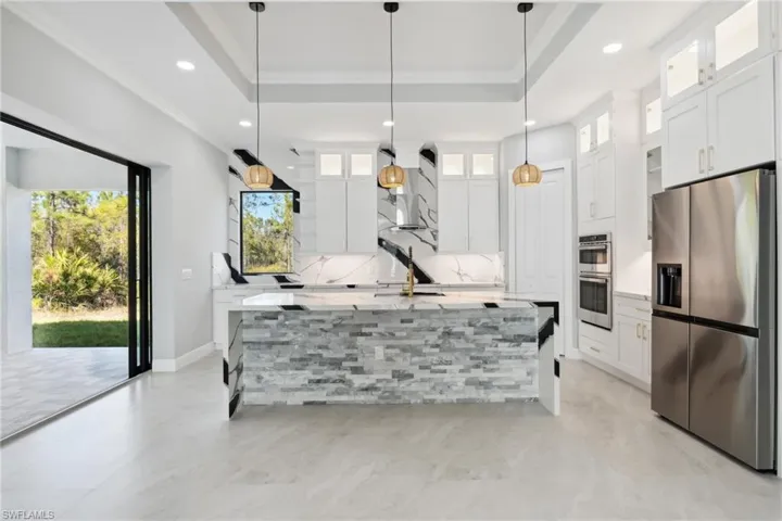 Kitchen with pendant lighting, white cabinets, stainless steel appliances, and a kitchen island with sink