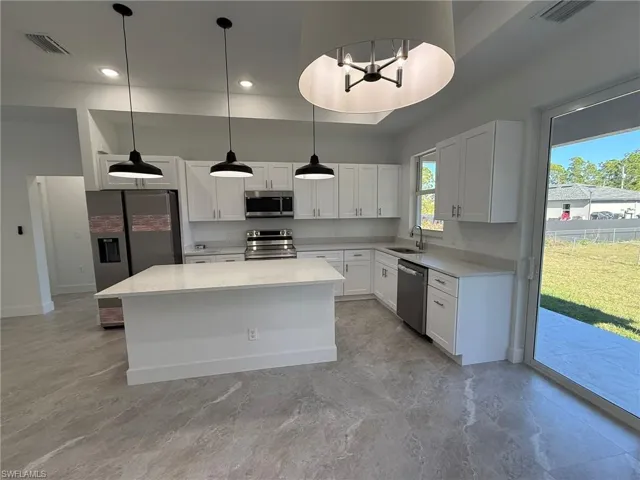 Kitchen featuring appliances with stainless steel finishes, white cabinetry, hanging light fixtures, light stone countertops, and a center island
