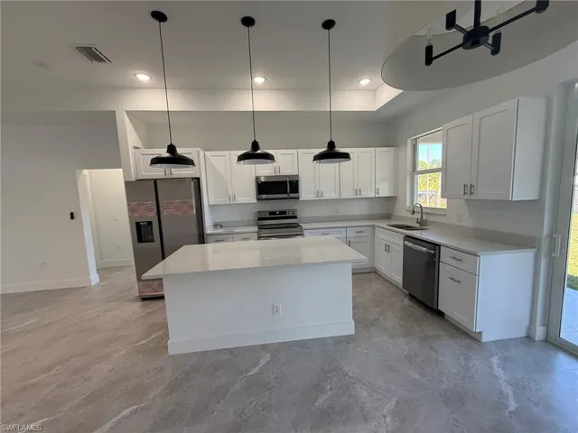 Kitchen featuring stainless steel appliances, light stone countertops, white cabinets, pendant lighting, and a kitchen island