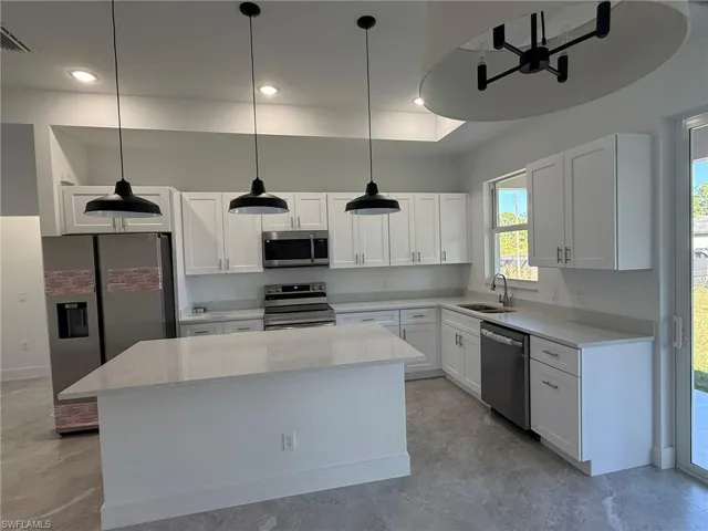 Kitchen featuring stainless steel appliances, light stone counters, white cabinets, a kitchen island, and hanging light fixtures