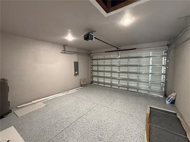 Garage with water heater, electric panel, a textured wall, and a garage door opener