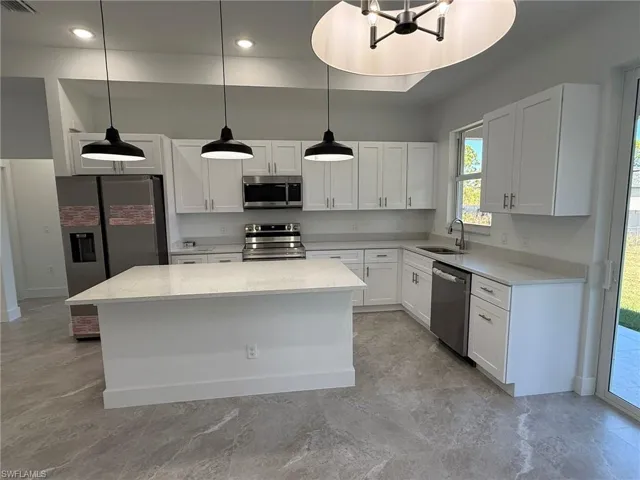 Kitchen with stainless steel appliances, light stone counters, a center island, and white cabinetry