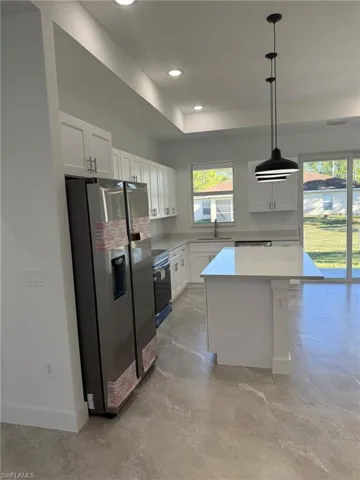 Kitchen with stainless steel fridge with ice dispenser, white cabinetry, pendant lighting, a kitchen island, and range with electric stovetop