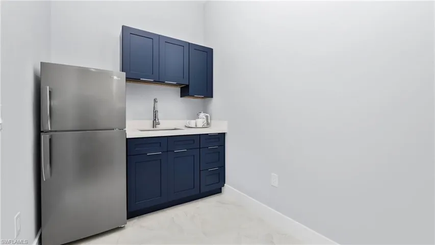 Bar featuring freestanding refrigerator, blue cabinetry, and light marble finish flooring