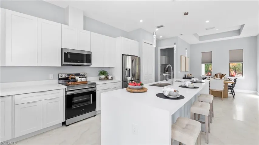 Kitchen featuring stainless steel appliances, a kitchen breakfast bar, pendant lighting, an island with sink, and light stone countertops