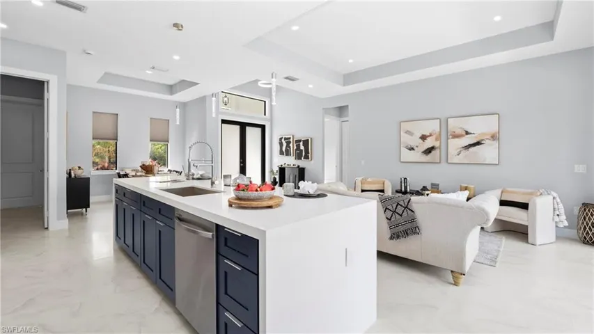 Kitchen featuring a raised ceiling, open floor plan, light stone countertops, dishwasher, and blue cabinets