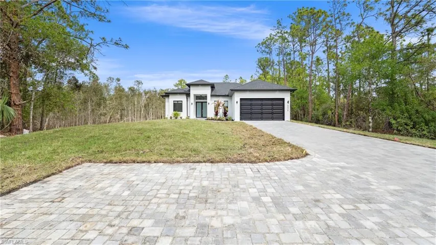 View of front facade featuring a front lawn, a garage, decorative driveway, and stucco siding