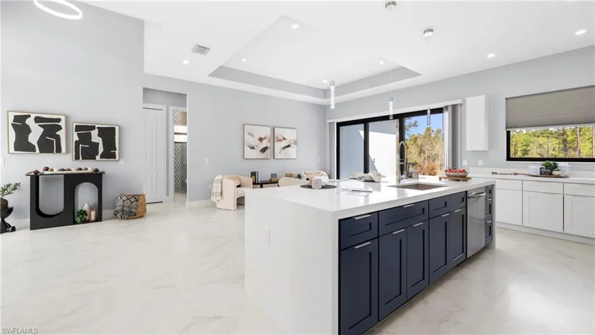Kitchen featuring pendant lighting, two tone cabinets, light stone countertops, a tray ceiling, and light marble finish flooring