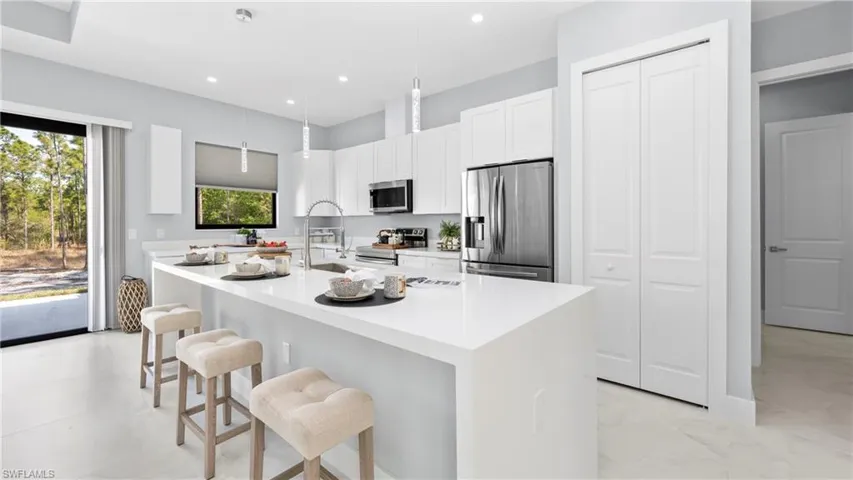 Kitchen featuring stainless steel appliances, a kitchen breakfast bar, decorative light fixtures, white cabinetry, and light stone counters