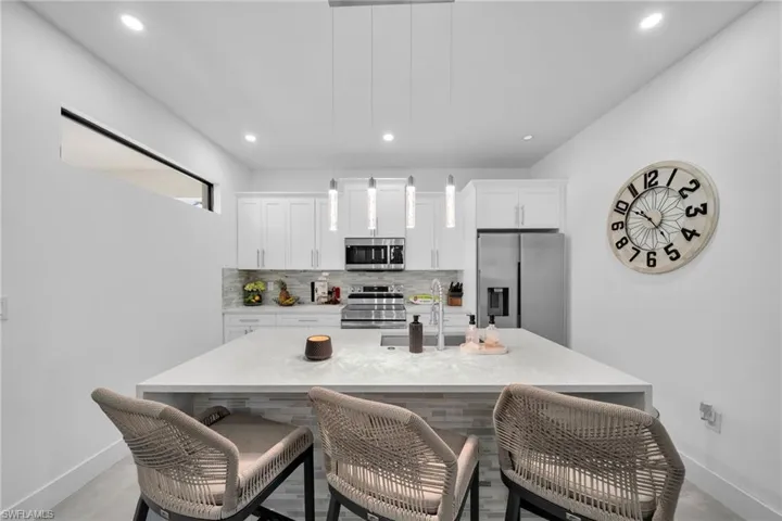 Quarts Counter tops Kitchen with appliances with stainless steel finishes, backsplash, a kitchen island with sink, a breakfast bar area, and recessed lighting