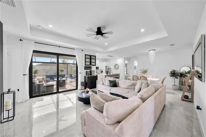 Living room featuring a tray ceiling, recessed lighting, light marble finish floors, and ceiling fan