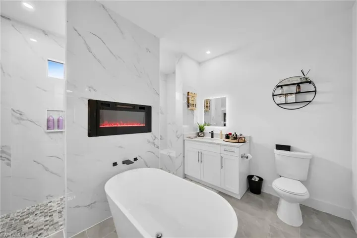 Bathroom with vanity, a freestanding bath, a high end fireplace, recessed lighting, and a marble finish shower