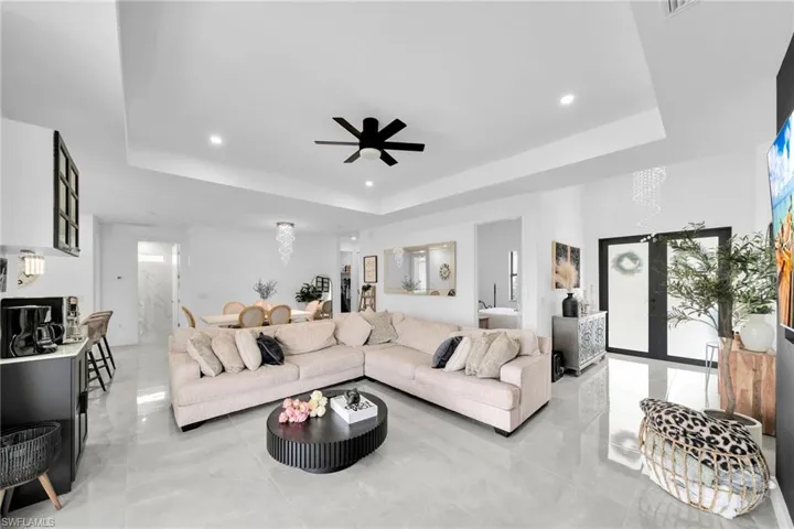 Living area with a tray ceiling, ceiling fan, recessed lighting, and light marble finish flooring