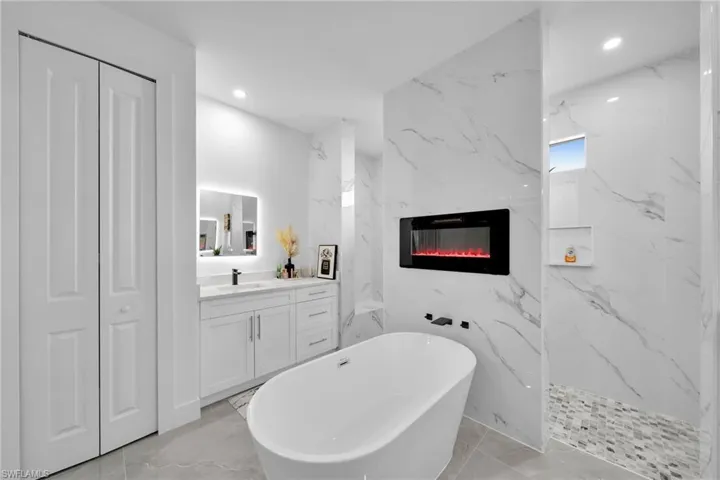 Full bathroom with a freestanding tub, vanity, a fireplace, marble tiled flooring, and a closet