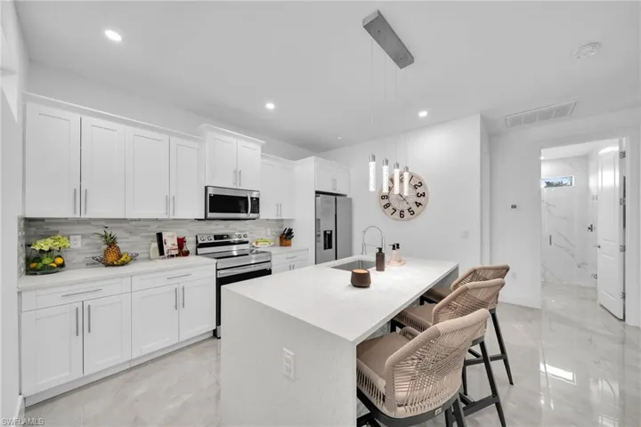 stainless steel appliances, an island with sink, a kitchen breakfast bar, recessed lighting, and white cabinetry
