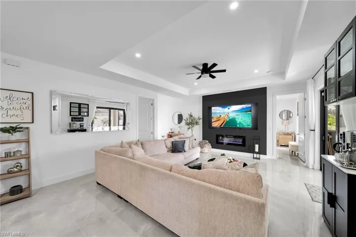 Living room with a tray ceiling, a ceiling fan, plenty of natural light, recessed lighting, and light marble finish flooring
