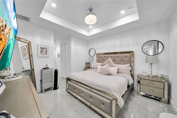 Bedroom with recessed lighting, marble finish floors, and a raised ceiling