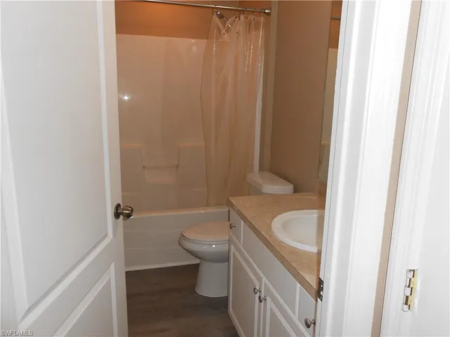 Bathroom featuring vanity, shower / bath combo with shower curtain, and dark wood-type flooring
