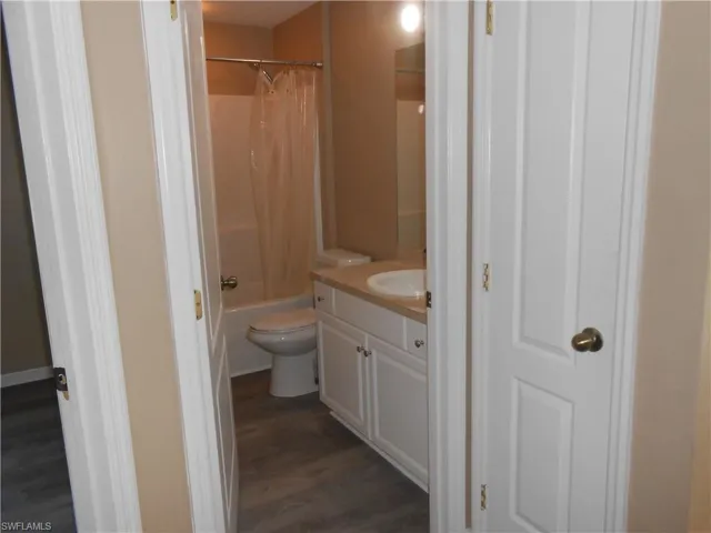 Full bath with vanity, shower / tub combo with curtain, and dark wood-style flooring