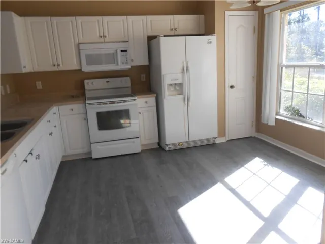 Kitchen with white appliances, white cabinets, dark wood finished floors, and light countertops