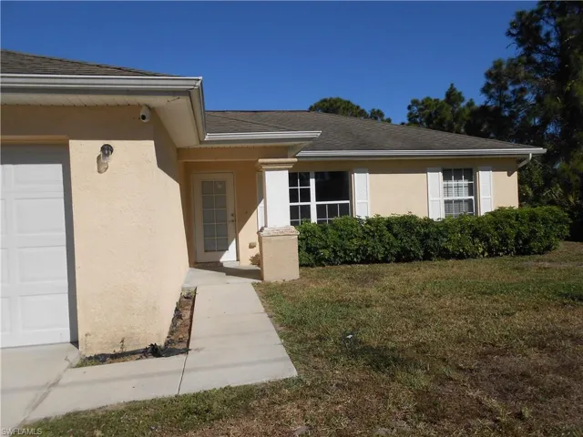 Property entrance with stucco siding, a yard, roof with shingles, and covered porch