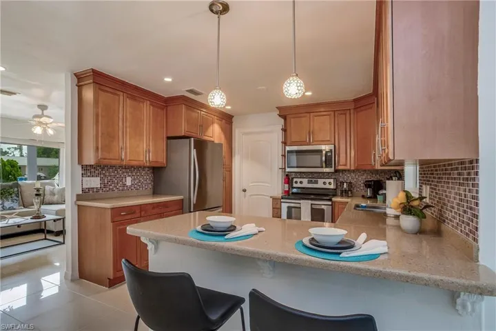 Kitchen with stainless steel appliances, a breakfast bar area, a peninsula, wood finish cabinetry, and hanging light fixtures