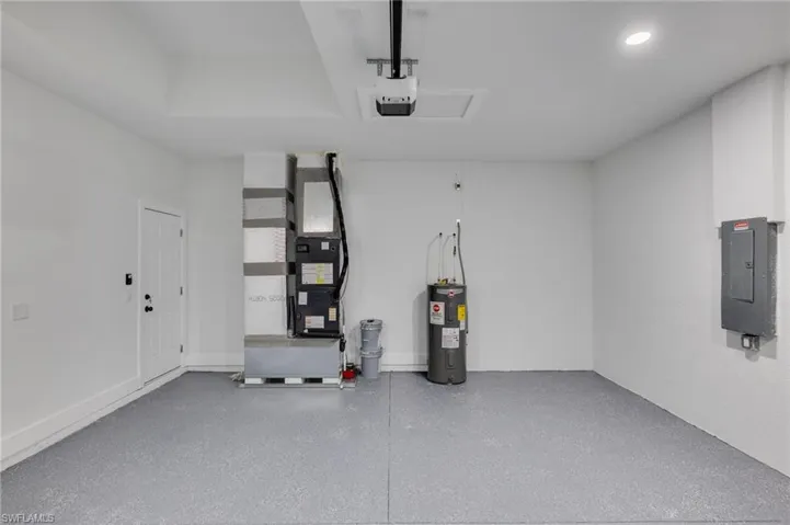 Garage featuring electric panel, water heater, heating unit, and a garage door opener