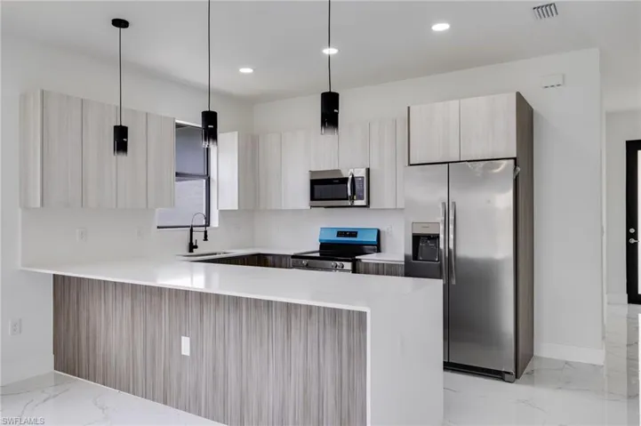Dual tone kitchen with stainless steel appliances, a peninsula, light stone countertops, modern cabinets, and two tone cabinets
