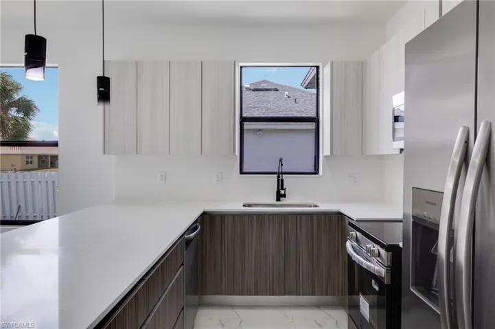 Dual tone kitchen featuring stainless steel appliances, modern cabinets, decorative light fixtures, two tone color scheme, and a peninsula