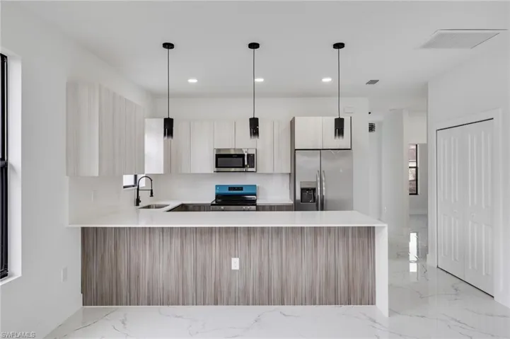 Kitchen with a peninsula, stainless steel appliances, light stone countertops, decorative light fixtures, and modern cabinets