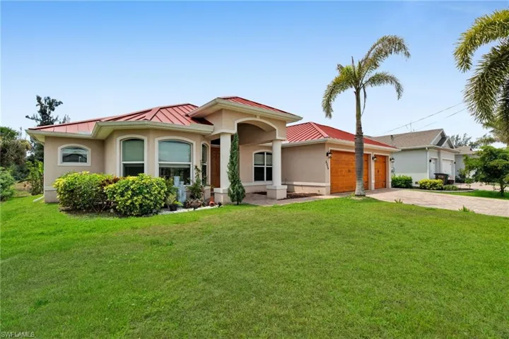 Mediterranean / spanish-style home featuring a standing seam roof, metal roof, driveway, stucco siding, and a front lawn