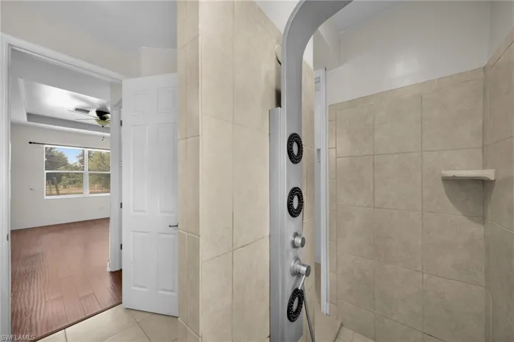 Full bath featuring tiled shower, ceiling fan, and tile patterned floors
